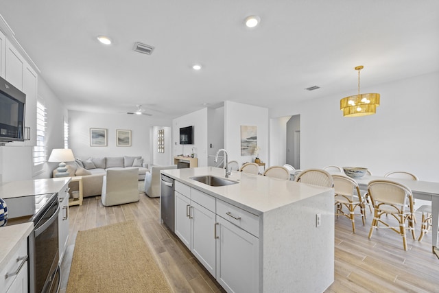 kitchen with white cabinets, sink, hanging light fixtures, an island with sink, and light hardwood / wood-style floors