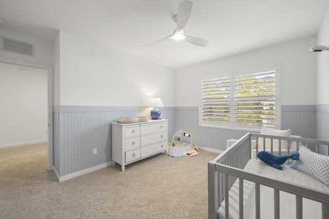 carpeted bedroom featuring a nursery area and ceiling fan