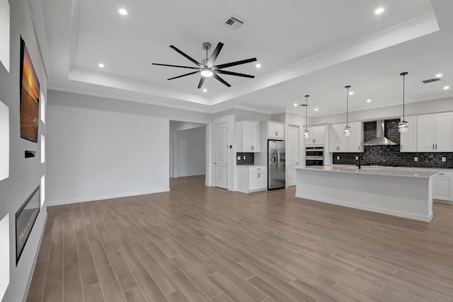 unfurnished living room featuring sink, a raised ceiling, ceiling fan, and light wood-type flooring