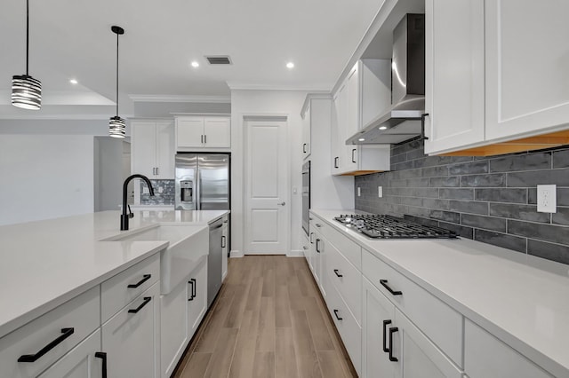 kitchen with wall chimney range hood, hanging light fixtures, light wood-type flooring, white cabinetry, and stainless steel appliances