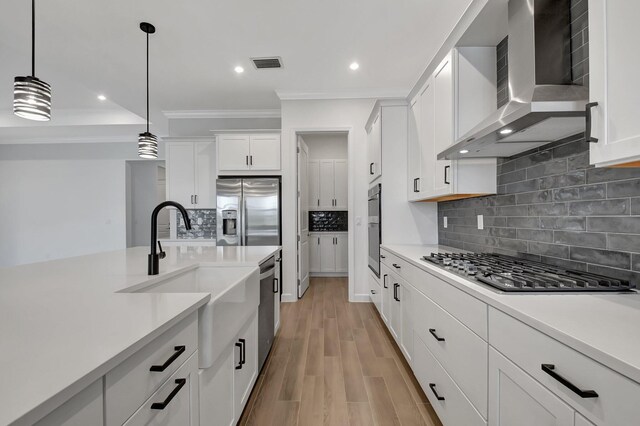 kitchen with appliances with stainless steel finishes, pendant lighting, white cabinetry, sink, and wall chimney exhaust hood