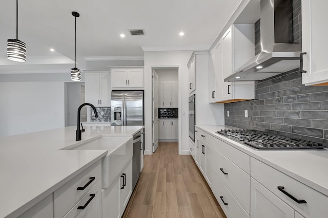 kitchen with sink, wall chimney exhaust hood, appliances with stainless steel finishes, light hardwood / wood-style floors, and white cabinetry