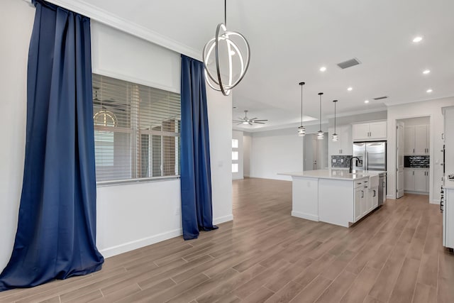 kitchen featuring white cabinetry, light hardwood / wood-style floors, hanging light fixtures, and a center island with sink