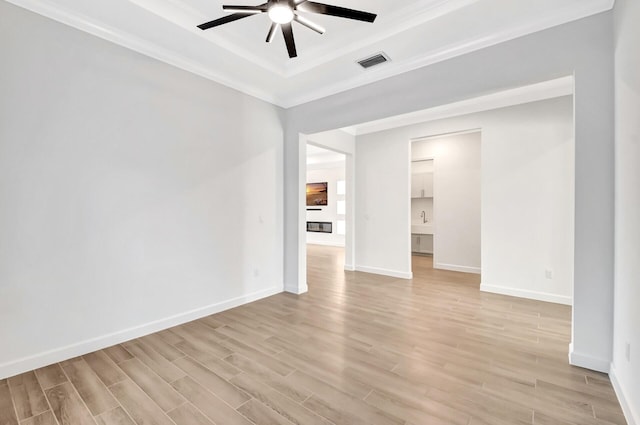 empty room with a raised ceiling, ceiling fan, crown molding, and light wood-type flooring