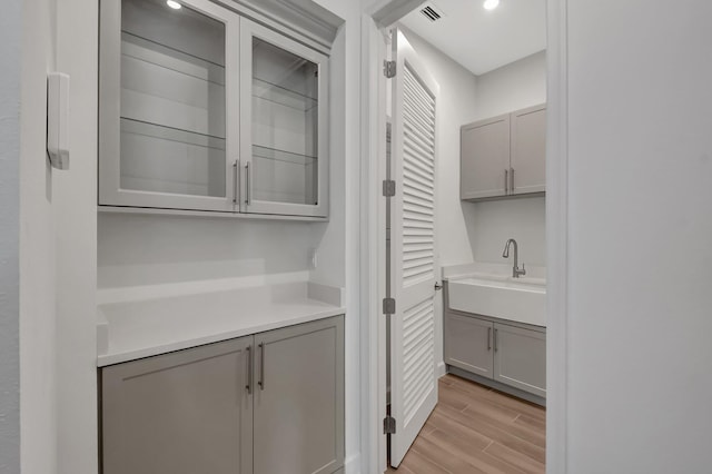 bar with gray cabinetry, light hardwood / wood-style flooring, and sink