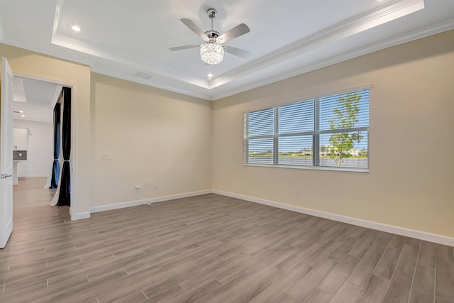 empty room with a tray ceiling, crown molding, ceiling fan, and light hardwood / wood-style floors