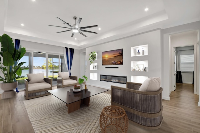 living room with a tray ceiling, ceiling fan, and light wood-type flooring