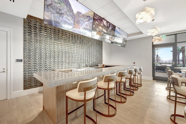 kitchen featuring a tray ceiling, light stone countertops, decorative light fixtures, and light hardwood / wood-style flooring