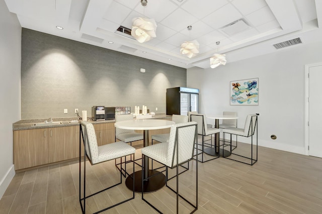 dining room featuring sink, a raised ceiling, and light hardwood / wood-style floors