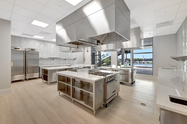 kitchen with high end appliances, decorative backsplash, a center island, and light stone countertops