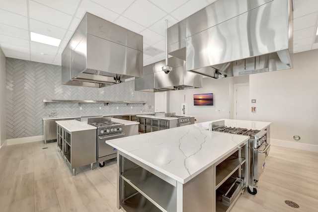 kitchen featuring gray cabinets, stainless steel range with gas stovetop, a center island, and exhaust hood