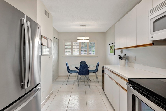 kitchen featuring hanging light fixtures, stainless steel fridge, a textured ceiling, light tile patterned flooring, and white cabinetry