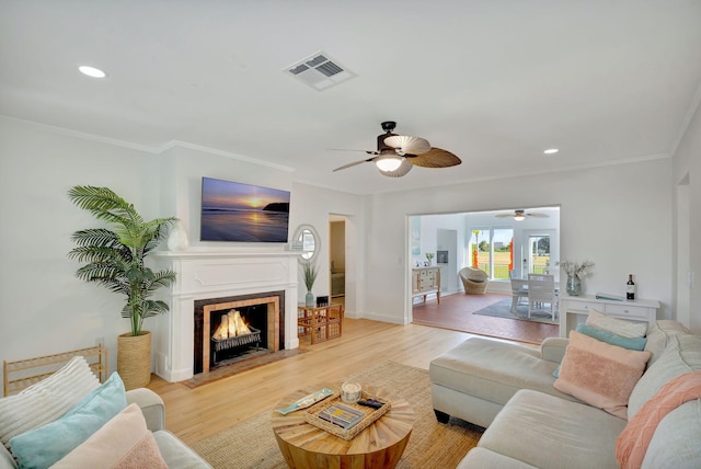 living room with light wood-type flooring, ornamental molding, and a tiled fireplace