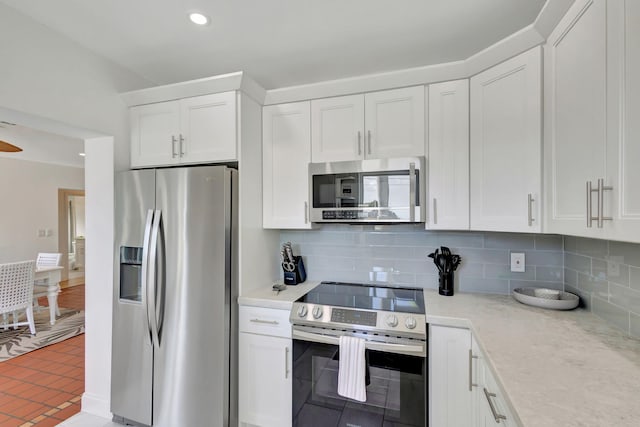 kitchen featuring appliances with stainless steel finishes, backsplash, light stone counters, tile patterned flooring, and white cabinetry