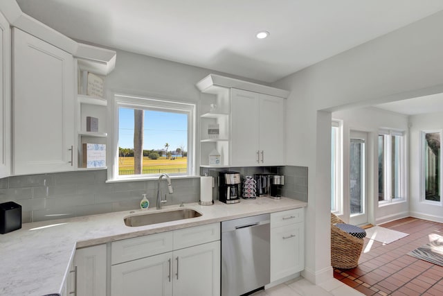 kitchen featuring open shelves, backsplash, stainless steel dishwasher, a sink, and white cabinetry