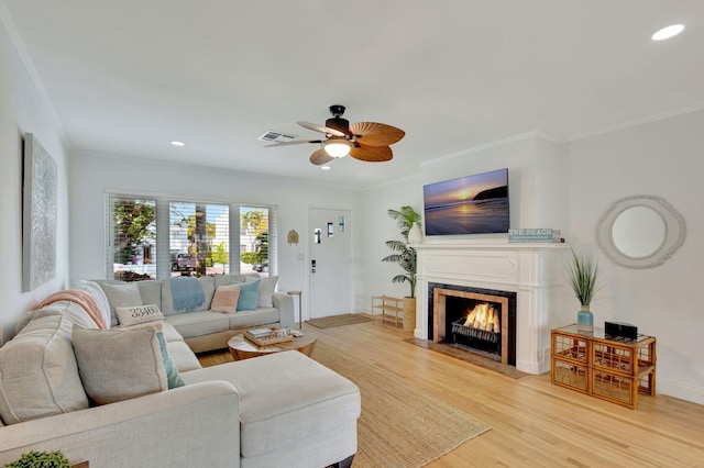 living area with a fireplace with flush hearth, recessed lighting, a ceiling fan, crown molding, and light wood-style flooring