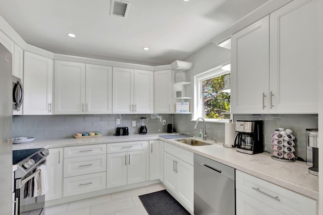 kitchen with a sink, white cabinetry, decorative backsplash, open shelves, and appliances with stainless steel finishes