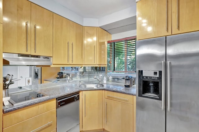 kitchen with appliances with stainless steel finishes, light brown cabinetry, dark stone countertops, and sink