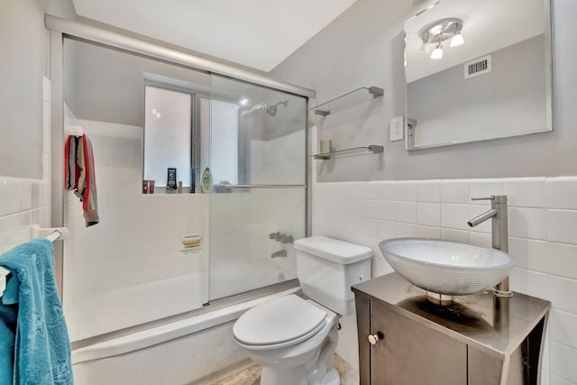 full bathroom with shower / bath combination with glass door, vanity, toilet, and tile walls