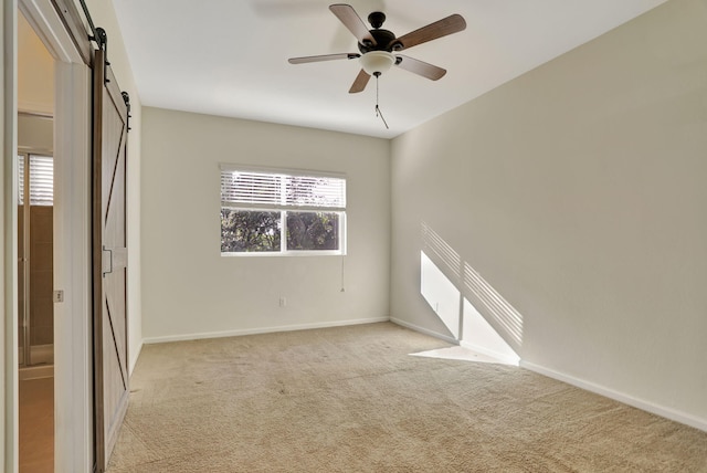 unfurnished room featuring ceiling fan, a barn door, and light colored carpet