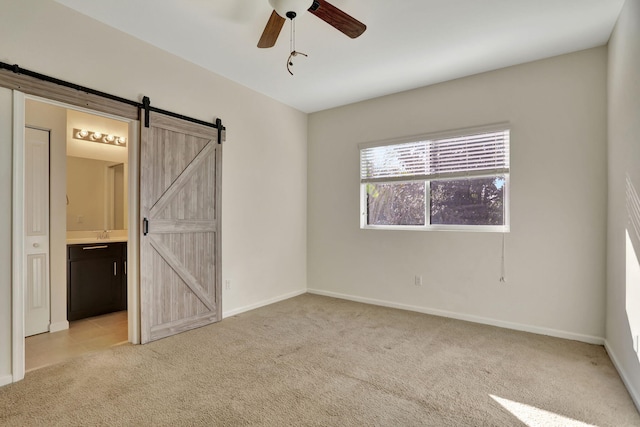 unfurnished bedroom with a barn door, light colored carpet, ceiling fan, and connected bathroom