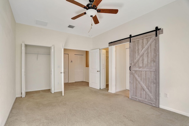 unfurnished bedroom featuring light carpet, a barn door, and ceiling fan