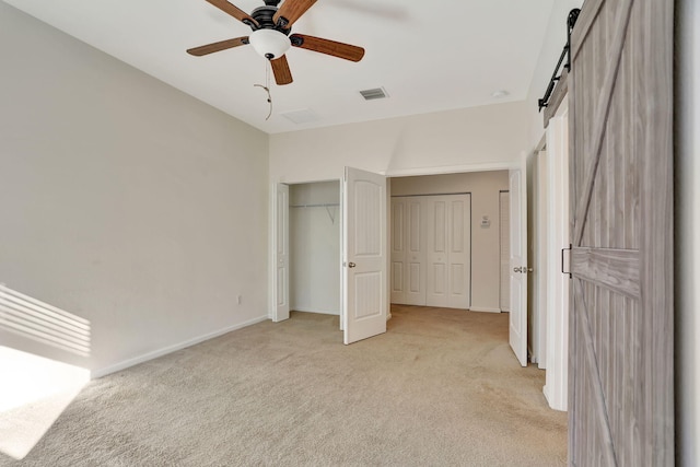 unfurnished bedroom featuring ceiling fan, a barn door, and light colored carpet