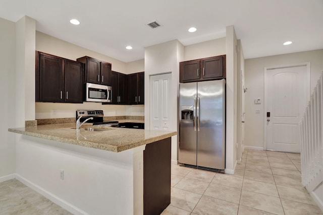 kitchen with kitchen peninsula, a kitchen bar, dark brown cabinetry, stainless steel appliances, and light tile patterned floors