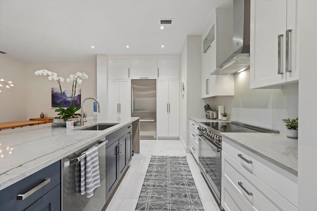 kitchen featuring light stone countertops, stainless steel appliances, sink, wall chimney range hood, and white cabinets