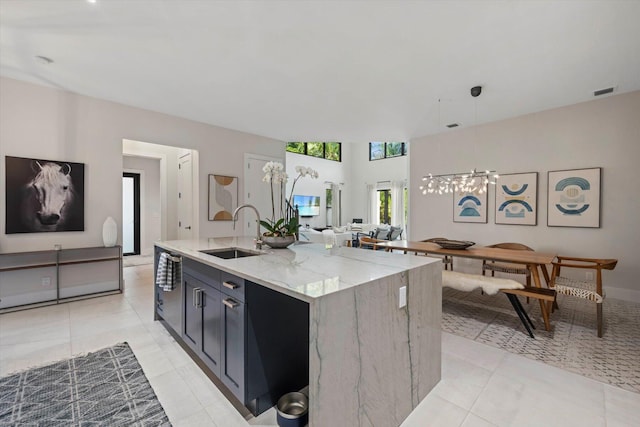 kitchen with light stone countertops, a kitchen island with sink, sink, light tile patterned floors, and decorative light fixtures