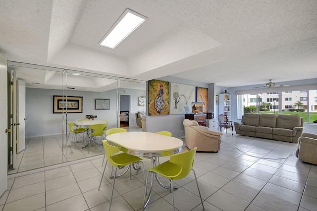 tiled dining space featuring a textured ceiling, a raised ceiling, and ceiling fan