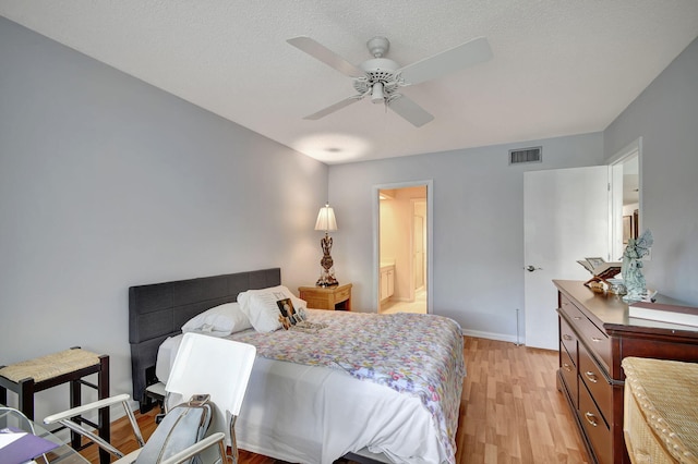 bedroom with a textured ceiling, light wood-type flooring, ceiling fan, and connected bathroom