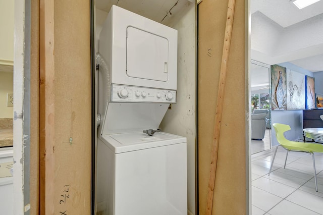 laundry area with light tile patterned flooring, stacked washing maching and dryer, and a skylight