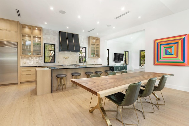 interior space featuring a kitchen breakfast bar, an island with sink, light brown cabinetry, light hardwood / wood-style floors, and stainless steel built in refrigerator