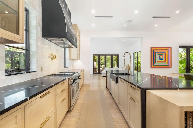 kitchen featuring light brown cabinetry, range with two ovens, a wealth of natural light, and wall chimney exhaust hood