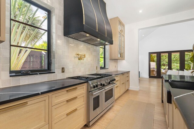 kitchen featuring premium range hood, light hardwood / wood-style floors, range with two ovens, decorative backsplash, and light brown cabinetry