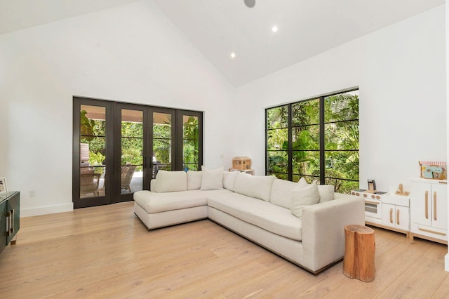 living room with plenty of natural light, high vaulted ceiling, french doors, and light wood-type flooring