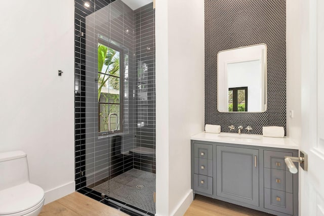 bathroom with tiled shower, vanity, hardwood / wood-style flooring, and toilet