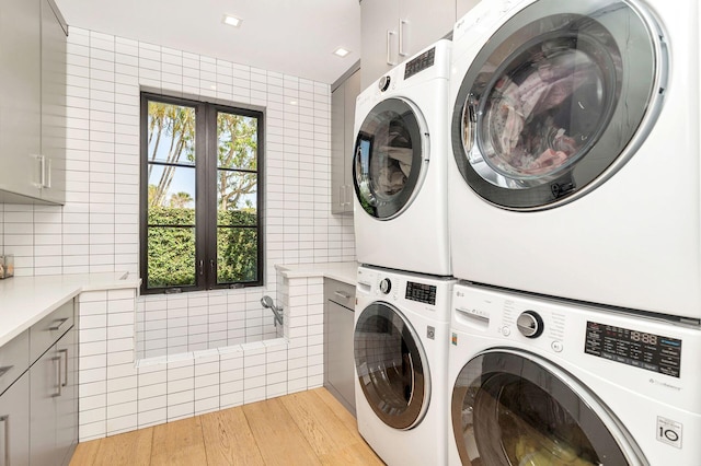 washroom with light hardwood / wood-style floors, cabinets, stacked washer and dryer, and washing machine and dryer