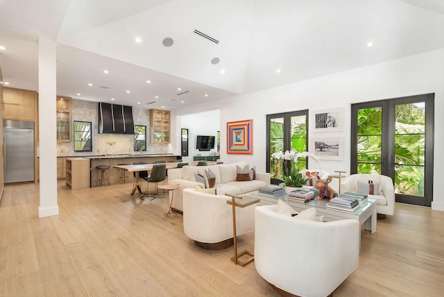 living room featuring light hardwood / wood-style floors, a healthy amount of sunlight, high vaulted ceiling, and french doors