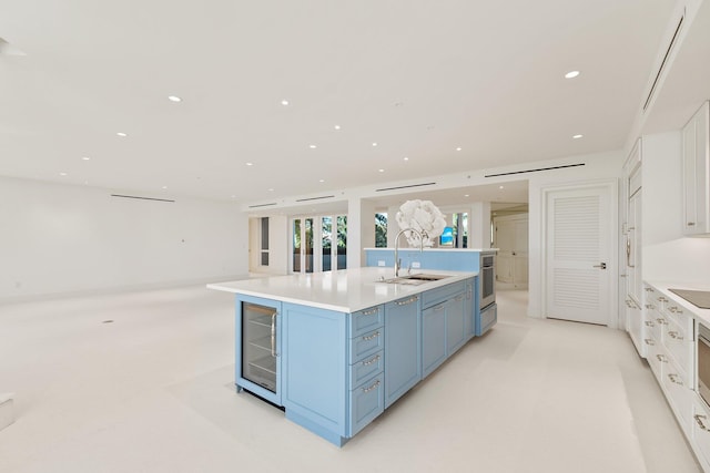 kitchen featuring white cabinets, blue cabinets, sink, and a kitchen island with sink