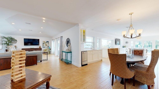 dining space with a notable chandelier, light wood-type flooring, sink, and vaulted ceiling