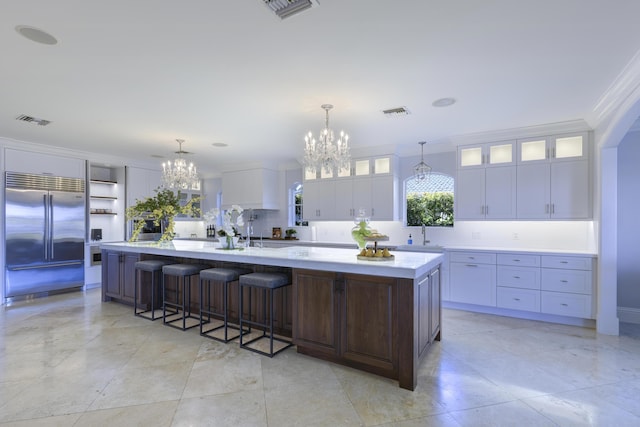 kitchen with a large island with sink, built in fridge, crown molding, decorative light fixtures, and white cabinetry