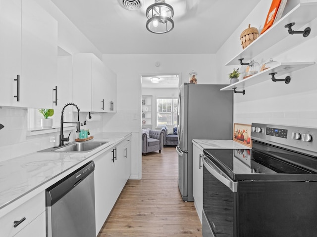 kitchen with sink, appliances with stainless steel finishes, light hardwood / wood-style floors, light stone counters, and white cabinetry