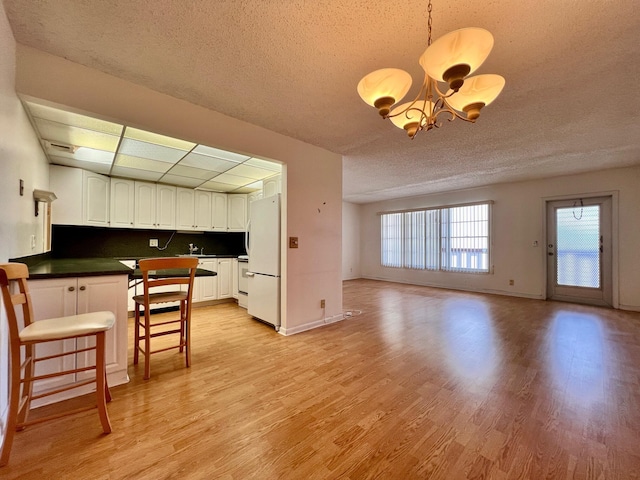 kitchen featuring decorative backsplash, a breakfast bar, white refrigerator, an inviting chandelier, and white cabinets