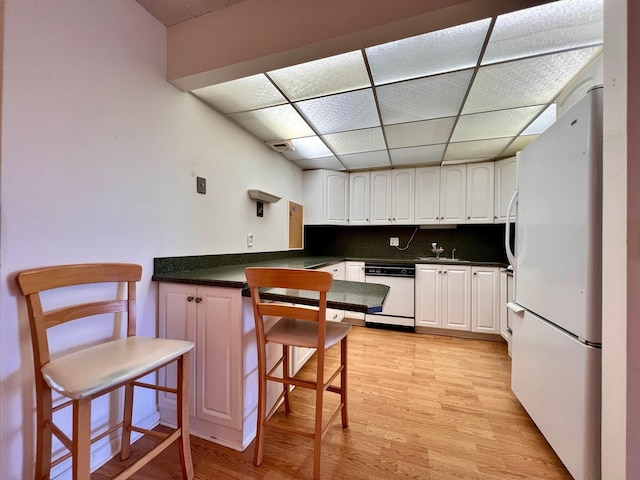 kitchen featuring a paneled ceiling, backsplash, a breakfast bar, white appliances, and white cabinets