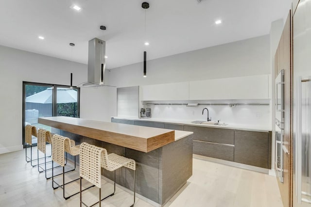 kitchen with light wood-type flooring, island range hood, sink, pendant lighting, and a center island