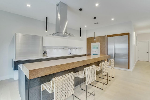 kitchen with built in refrigerator, island range hood, sink, and pendant lighting