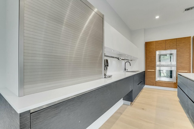 kitchen featuring light hardwood / wood-style flooring, sink, multiple ovens, and built in microwave