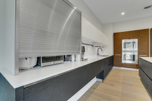 kitchen with built in microwave, sink, double wall oven, and light hardwood / wood-style flooring